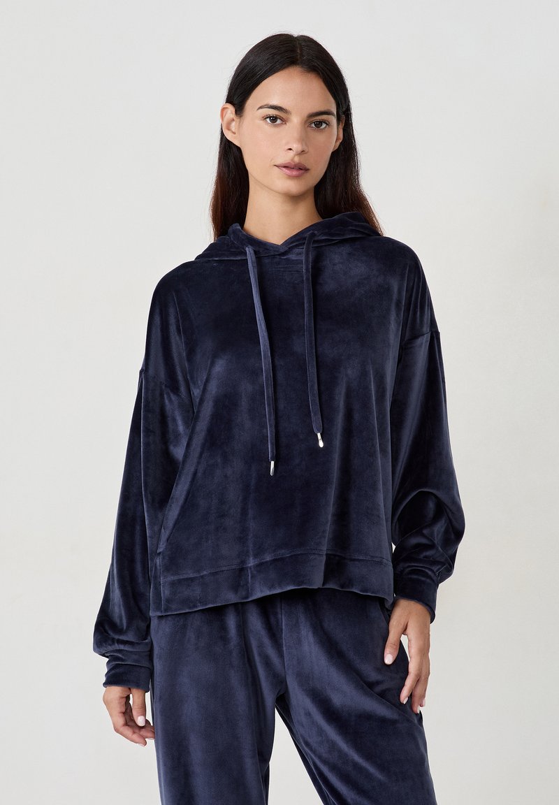 Granatowy welurowy hoodie o luźnym kroju, z długimi rękawami i kapturem ze sznurkiem. Posiada gładką fakturę i prążkowane akcenty na dole.