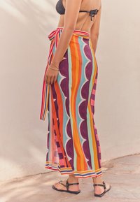 Colorful, striped maxi skirt with varying widths of stripes in orange, purple, and teal. Features a tied waistband and slit detail.