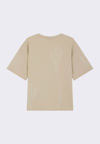 Camiseta de manga corta beige con bordado de cactus blanco en el frente y las mangas, hecha de material de algodón suave, con un corte relajado.