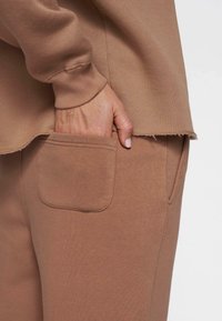 Brune sweatpants med en sidelomme og et blødt, tekstureret stof med en rå kantdetalje nederst på toppen.