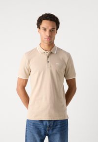 Beige polo skjorte med klassisk krage, tre knapper og kontrasterende hvit trim på kragen og ermene. Logo brodert på brystet.