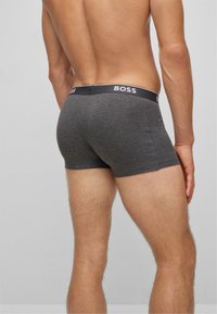 Graue Baumwollboxershorts mit einem schwarzen elastischen Bund, der den Markennamen "BOSS" in Weiß trägt. Der Stoff sieht weich und glatt aus.