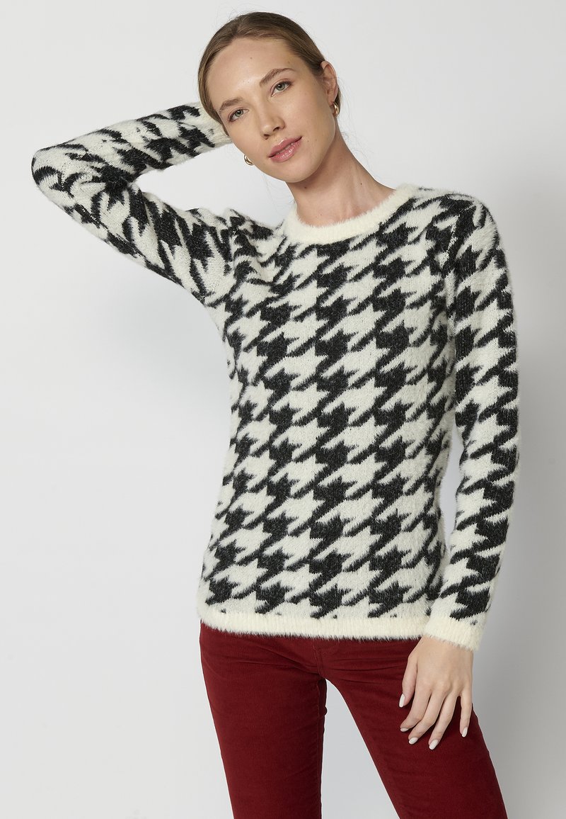 Pulover cu model houndstooth alb-negru, realizat dintr-un material moale și pufoș, având mâneci lungi și un guler rotund.