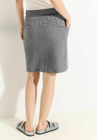 Jupe rayée avec un motif bleu marine et blanc, dotée d'une taille haute, de poches arrière et d'une coupe à mi-genou, associée à des chaussures argentées à enfiler.