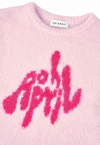 Ružičasti pleteni pulover s dlakavim ružičastim logom "OH APRIL" sprijeda, okruglim izrezom i rebrastim manžetama. Mekana tekstura s vidljivim vlaknima.