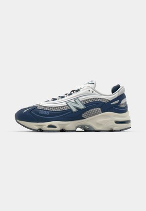 New Balance 1000 sneakers in navy and gray mesh, featuring a cushioned sole, textured accents, and prominent logo on the side.