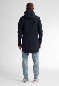 Granatowa wodoodporna kurtka z kapturem, długimi rękawami i zapinanymi mankietami. Połączona z jasnoniebieskimi dżinsami i białymi trampkami.