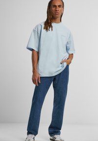 Camiseta oversize de color azul claro con mangas cortas, acompañada de jeans rectos de color azul oscuro y zapatillas blancas con rayas negras.