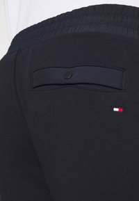 Námořnické tepláky mají hladkou látku, elastický pas, zadní kapsu na knoflík a malé logo v červené, bílé a modré barvě.