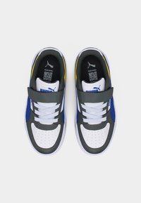 Ζευγάρι λευκών, γκρι και μπλε αθλητικών παπουτσιών Puma με λουράκια Velcro και κορδόνια, από πάνω σε φωτεινό φόντο.