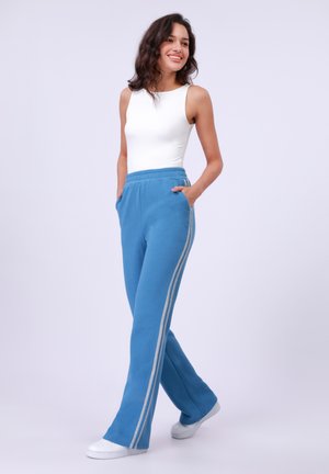 Light blue sweatpants with a relaxed cut, side pockets, and silver stripes along the sides. Paired with a fitted white tank top.