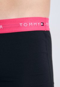 Boxer shorts en coton noir avec une ceinture élastique rose vif portant le logo "TOMMY" et de petits accents de logo en bleu et blanc.