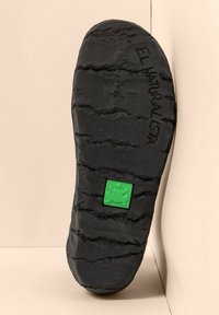 Suela de zapato negra con surcos profundos, un cuadrado verde con un logo de rana cerca del centro y "EL NATURALISTA" grabado a lo largo del lado.