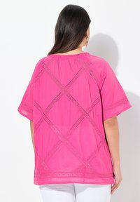 Maglietta fucsia a maniche corte con un fit rilassato, caratterizzata da dettagli in pizzo incrociato sul retro e un colletto arricciato.