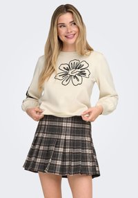 Kremfarvet sweater med sort blomstret broderi, kombineret med en plisseret ternet nederdel i brune, beige og sorte toner. Blød tekstur og pasform.