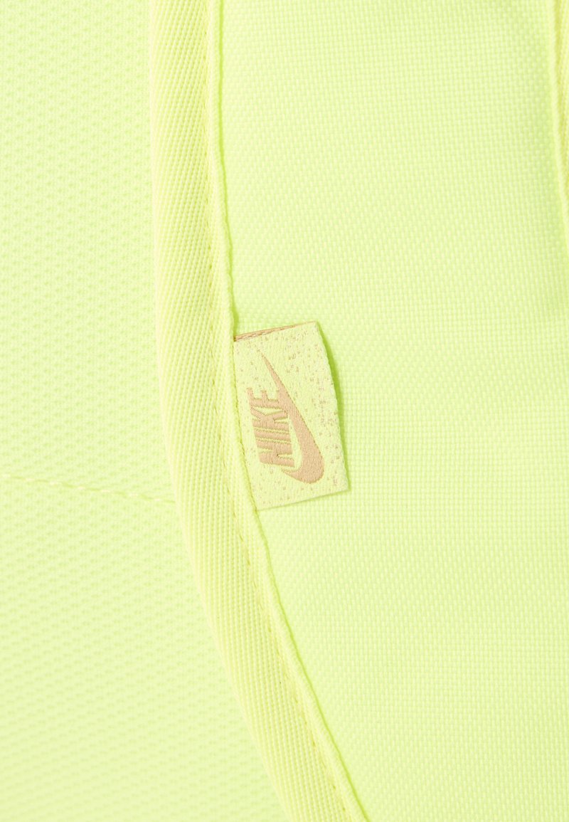 Tela amarillo neón con una costura cosida y una pequeña etiqueta beige de Nike que muestra el logo de la marca y el swoosh.