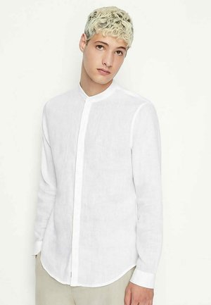 Camicia bianca in lino a maniche lunghe con colletto stand, chiusura a bottoni e una vestibilità rilassata, caratterizzata da una texture morbida e un design minimalista e liscio.