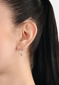 Silvrig hoops örhänge som visas på en människas öra. Örhänget har en slät, glänsande yta och en cirkulär form, vilket förstärker en minimalistisk design.