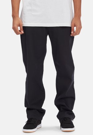 Black cotton pants with a relaxed fit, featuring a smooth texture and front pockets. Paired with black sneakers and a white t-shirt.