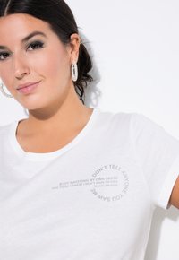Witte katoenen t-shirt met een ronde grafische tekstontwerp in grijs. Korte mouwen en een ronde halslijn. Soepele textuur.