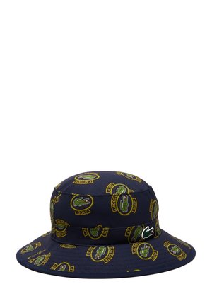 Chapeau seau marine en tissu, arborant un motif à logo Lacoste golf sur l'ensemble en vert et jaune. Texture douce avec un large bord.