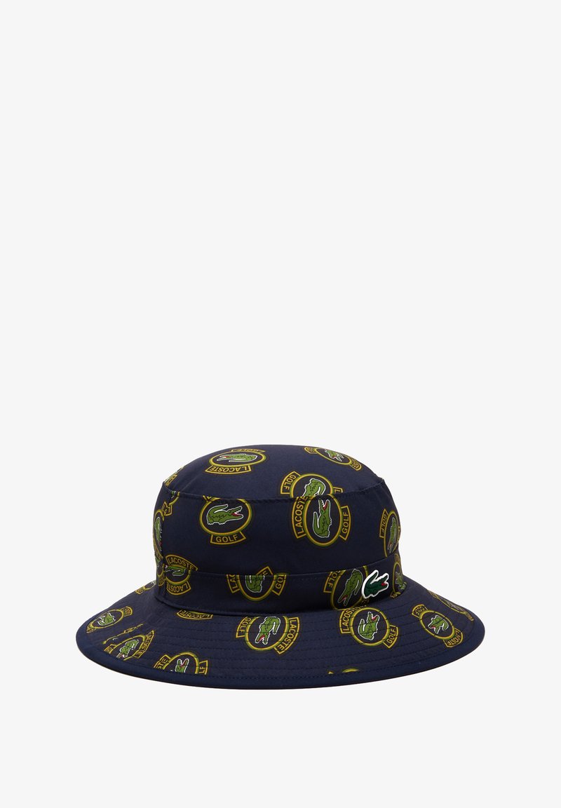 Chapeau seau marine en tissu, arborant un motif à logo Lacoste golf sur l'ensemble en vert et jaune. Texture douce avec un large bord.