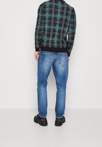 Sweter w czarno-morską kratę z prążkowanym dekoltem, zestawiony z jasnoniebieskimi dżinsami i czarnymi butami, widziany od tyłu.