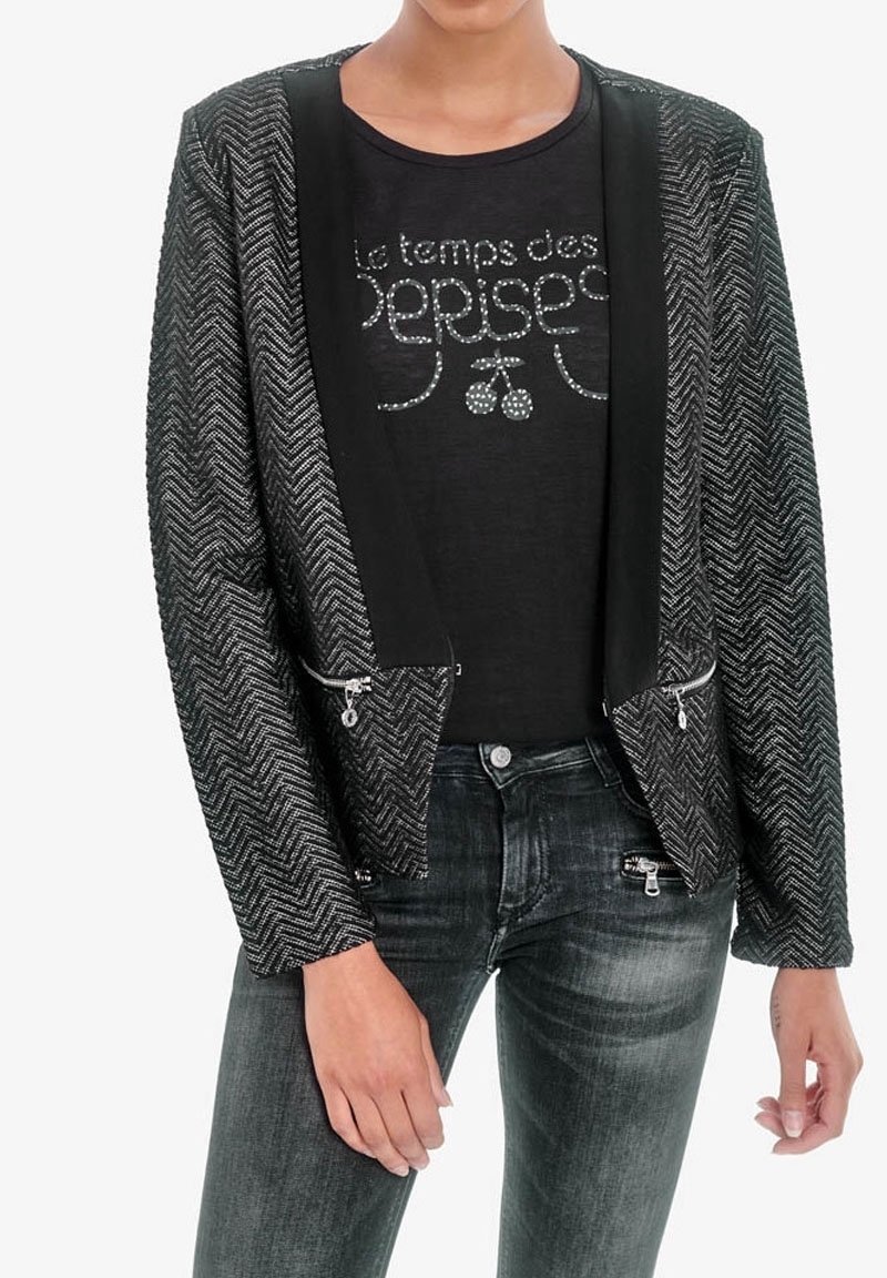 Černá krátká bunda s rybím vzorem, kontrastní saténové klopy a stříbrné kapsy na zip, spárovaná s černým tričkem s potiskem a tmavými džínami.