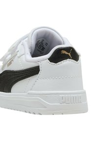 Zapatilla blanca con acentos negros y logo dorado, con parte superior de cuero suave, lengüeta acolchada y suela texturizada para mayor agarre.