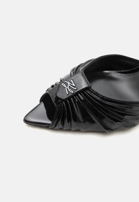 Μαύρο πλατίνι παπούτσι με μυτερή μύτη και επίπεδη σόλα, με πιετέ λεπτομέρειες και ασημένιο διακοσμητικό κούμπωμα στο μπροστινό πάνω μέρος.