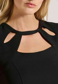Schwarzes Kleid mit einem semi-transparenten Ausschnitt und Ausschnitten, sowie einer glatten Textur. Das Design betont den Bereich des Schlüsselbeins.