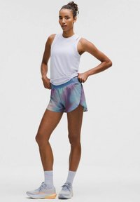 Träningsoutfit som består av en vit ärmlös topp, flerfärgade tie-dye shorts och ljusgrå sneakers med orangea detaljer.