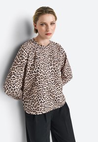 Leopardenmuster Bluse aus weichem Stoff, mit langen Ärmeln und rundem Halsauschnitt, kombiniert mit schwarzen Hosen vor einem neutralen Hintergrund.