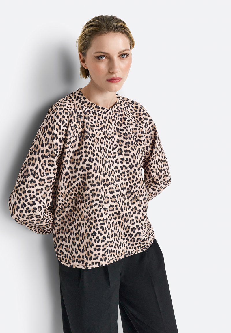 Leopardenmuster Bluse aus weichem Stoff, mit langen Ärmeln und rundem Halsauschnitt, kombiniert mit schwarzen Hosen vor einem neutralen Hintergrund.