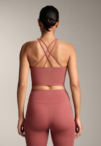 Top de sport roz zmeură cu bretele încrucișate; asociat cu leggings strâmți cu talie înaltă. Material neted și elastic; logo prezent.