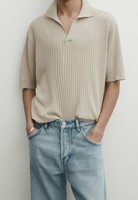 Beige ribbattu polo-paita kauluksella, yhdistettynä vaaleansinisiin farkkuihin. Paidassa on lyhyet hihat ja rento istuvuus.