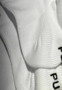 Weiße Baumwoll-Söckchen mit strukturiertem Ripp, gefaltet, mit schwarzem Text am Rand. Glatte Oberfläche und weicher Stoff.