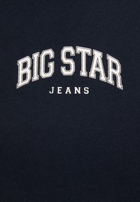 Námořnická modrá tkanina s textem "BIG STAR" psaným tučným bílým písmem ve tvaru oblouku nad "JEANS" v menších písmenkách, což vytváří výrazný design.