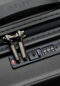 Valigia rigida nera con cerniera, cursori in metallo nero, serratura combinata TSA e superficie strutturata con il logo Delsey.
