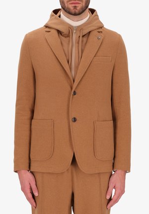 Blazer in lana color cuoio con rever a notched, due tasche frontali e chiusura con un solo bottone; indossato sopra un hoodie con zip coordinato in color cuoio.
