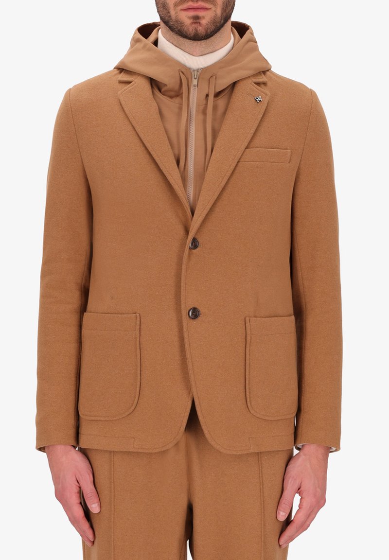 Blazer in lana color cuoio con rever a notched, due tasche frontali e chiusura con un solo bottone; indossato sopra un hoodie con zip coordinato in color cuoio.