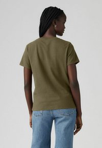 Camiseta de algodón verde oliva con mangas cortas y escote redondo, combinada con jeans de mezclilla azul claro. Vista trasera sencilla, sin patrones ni acentos.