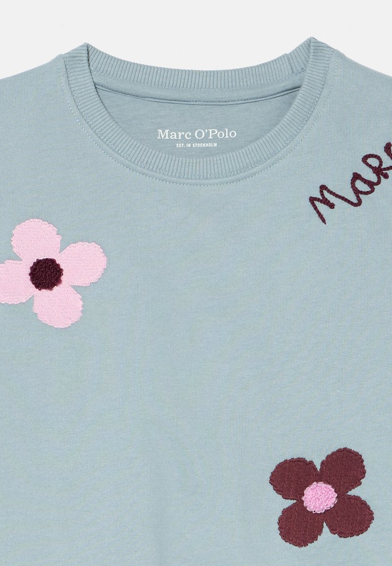 Jasnoniebieska bluza z haftowanymi kwiatami: jeden różowy z ciemnym środkiem, drugi burgundowy z jaśniejszym środkiem. Widoczna metka "Marc O'Polo".