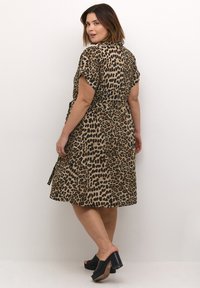 Robe imprimée léopard en tissu léger, manches courtes, taille ceinturée, jupe fluide. Portée avec des chaussures à enfiler noires à plateforme.