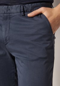 Navyblå byxor i ett slätt, lätt tyg. Har sidofickor och en slim fit-design med en subtil lyster.