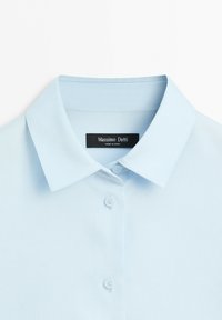 Světlá modrá košile s límečkem, knoflíky a viditelnou značkou u krku s nápisem Massimo Dutti.