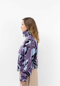 Lila und hellblaue Fleecejacke mit hohem Kragen, ausgestattet mit einem Camouflage-Muster und einer Fronttasche. Lange Ärmel mit Logodetail an der Seite.
