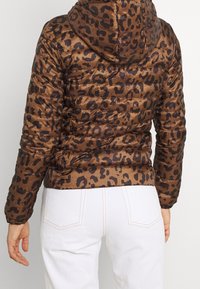 Giacca imbottita marrone con stampa leopardata e cappuccio, caratterizzata da un design trapuntato e orlo elastico. Il materiale sembra liscio e lucido.