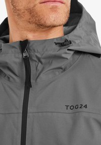 Gray waterproof jacket featuring a high collar, adjustable hood with toggle, and black zipper, with "TOG24" logo on the front.