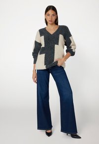 Maglione a V con un audace motivo geometrico bianco e nero, abbinato a jeans a gamba larga blu scuro e tacchi neri a punta.